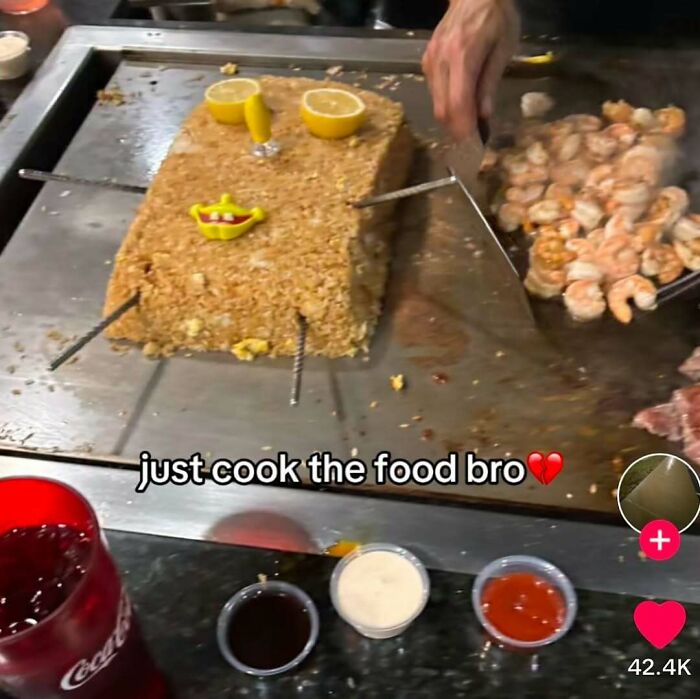 A block of rice decorated with lemon and face toys on a grill next to cooked shrimp, implying bizarre cooking skills.