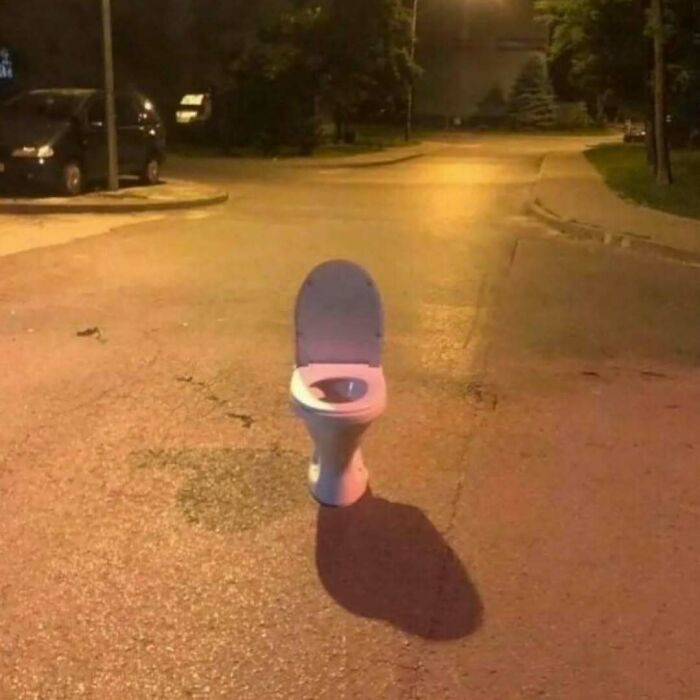 Toilet bowl standing alone in the middle of an empty street at night, an unusual image that might need a priest or exorcist.