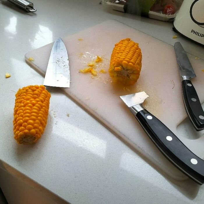 Two corn cobs cut into halves on a cutting board with kitchen knives, an image that might need a priest or an exorcist.