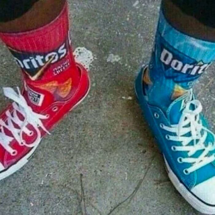 Mismatched red and blue sneakers with colorful Doritos-themed socks on a concrete surface, strange footwear combination.