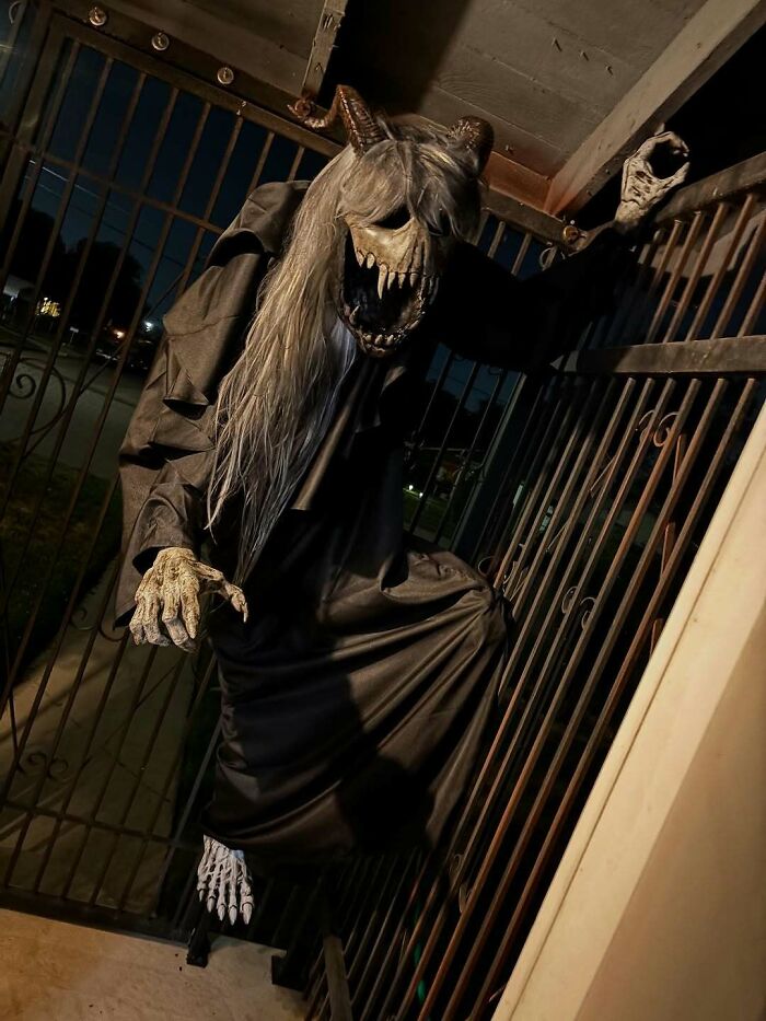 Horror-themed outdoor Halloween decoration with a demonic figure climbing a gate at night, showcasing spooky Halloween decor.