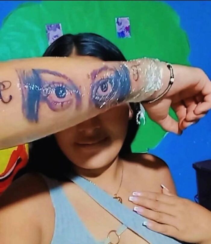 Person showing an awkward tattoo of blue eyes on their forearm, highlighting awful tattoos and questionable decisions.