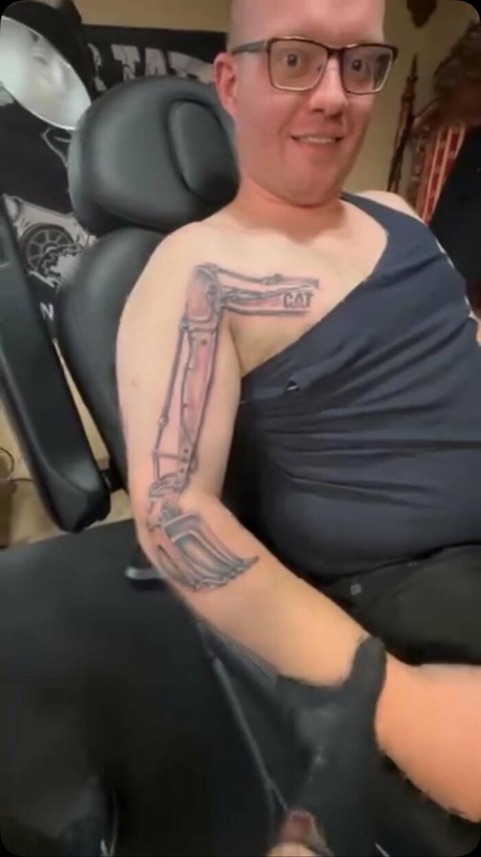 Man sitting in a chair showing an awkward mechanical arm tattoo, illustrating awful tattoos and poor decisions.