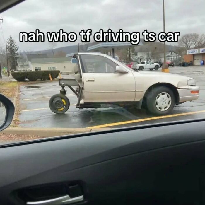 Beige car missing front wheels, replaced with a single small wheel, parked in an empty lot, a strange image needing an exorcist.