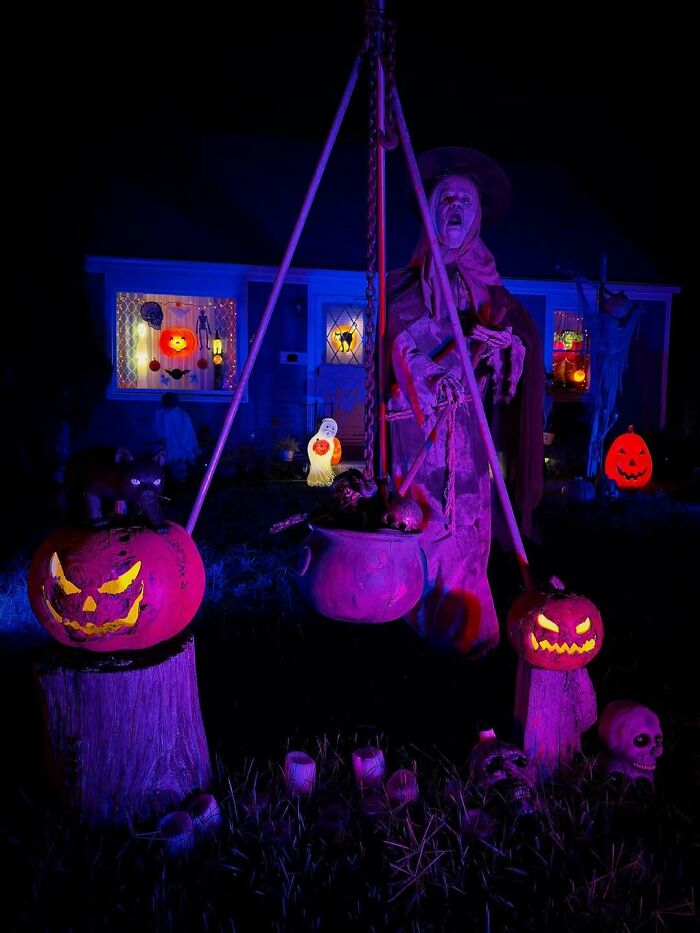 Spooky outdoor Halloween decorations featuring glowing jack-o-lanterns, skulls, and a witch figure at night.