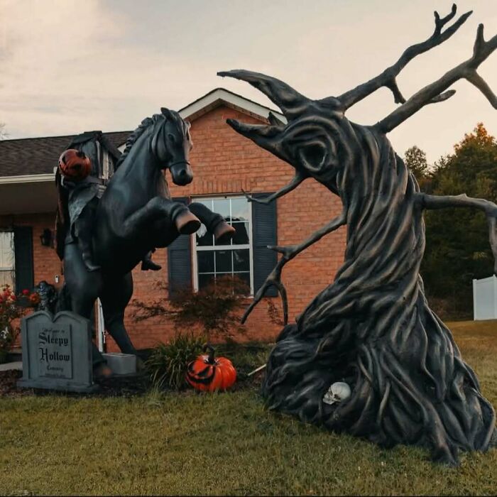Outdoor Halloween decorations featuring a spooky headless horseman, a twisted tree, pumpkins, and a Sleepy Hollow sign.
