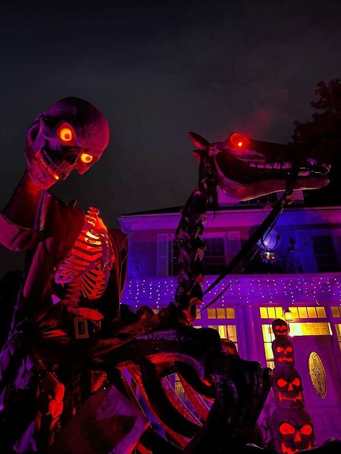 Skeleton and horse with glowing red eyes as outdoor Halloween decorations lit up in purple and orange lights at night.