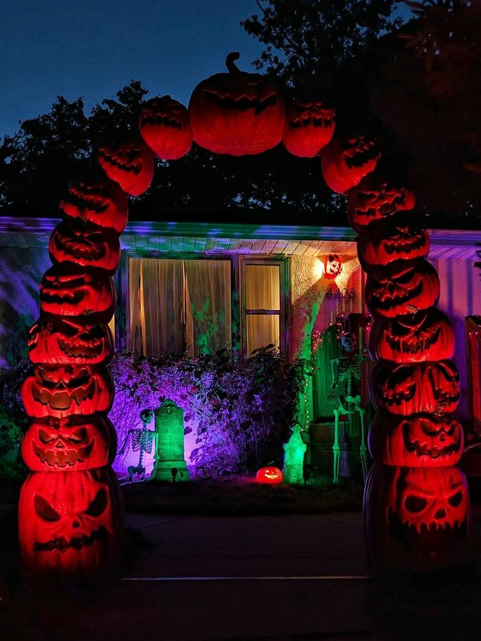 Glowing outdoor Halloween decorations with a large arch of stacked jack-o'-lanterns and spooky yard display at night.