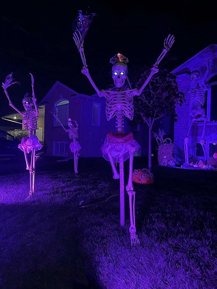 Glowing skeletons in tutus pose outdoors in a creative Halloween decoration display at night.