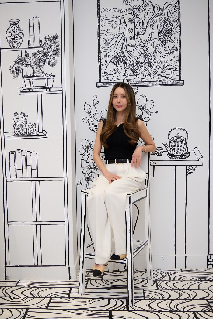 Woman sitting in a 2D restaurant in NYC with black and white drawing-style walls and furniture creating an optical illusion. Woman sitting in a 2D restaurant in NYC with black and white drawing-style walls and furniture creating an optical illusion.