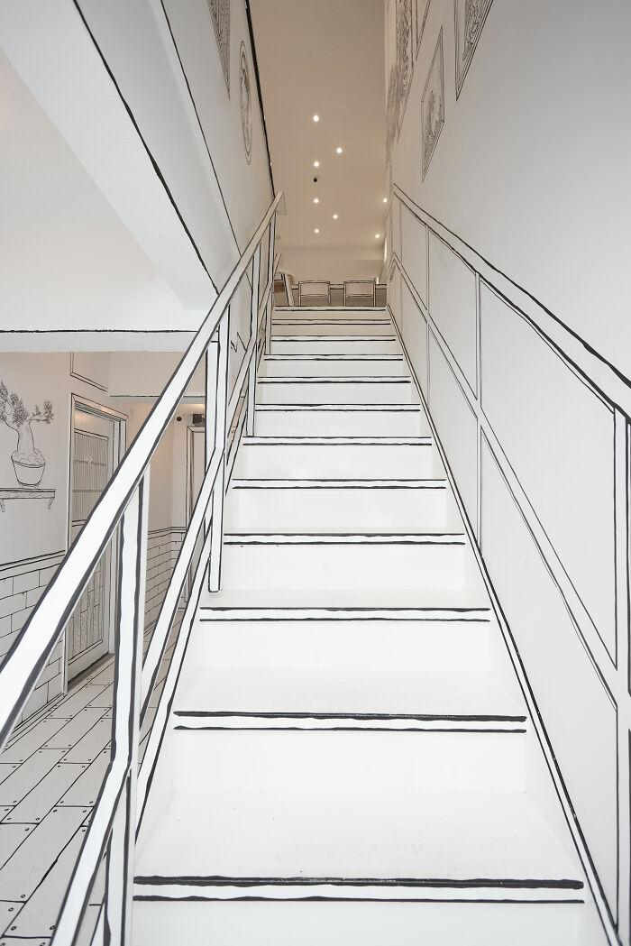 Staircase inside a 2D restaurant in NYC with black outlined white walls and railings resembling a drawing. Staircase inside a 2D restaurant in NYC with black outlined white walls and railings resembling a drawing.