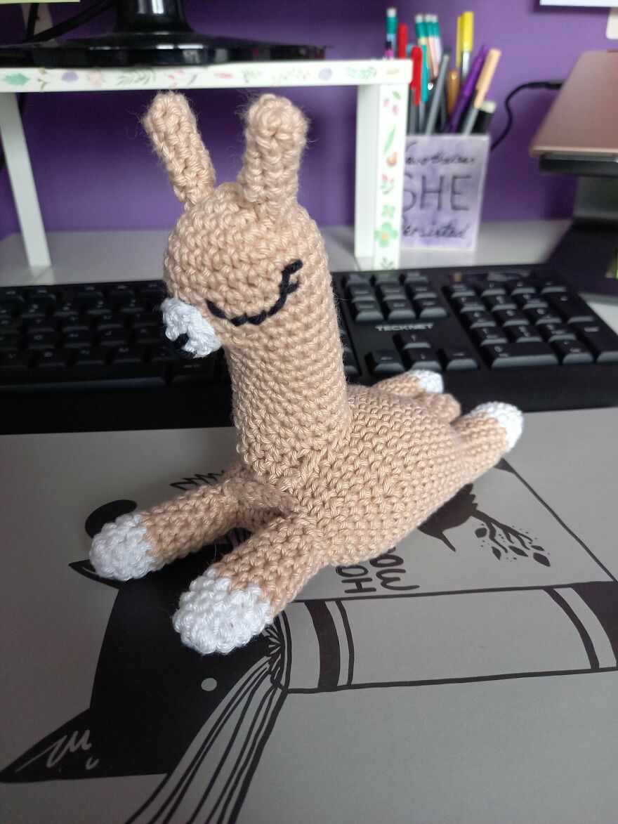 Beige crochet animal with white paws, resting on a desk in front of a computer keyboard, showcasing crochet animals personality.