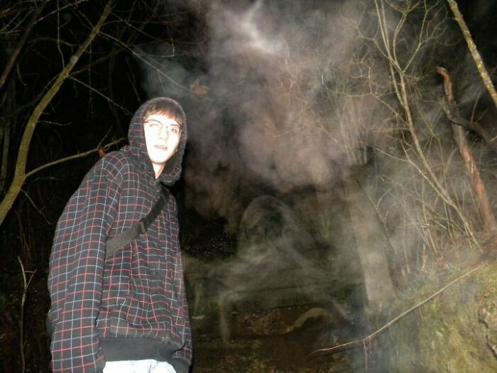 A young person in a hoodie stands in a dark forest surrounded by creepy fog, creating a chilling photo moment.
