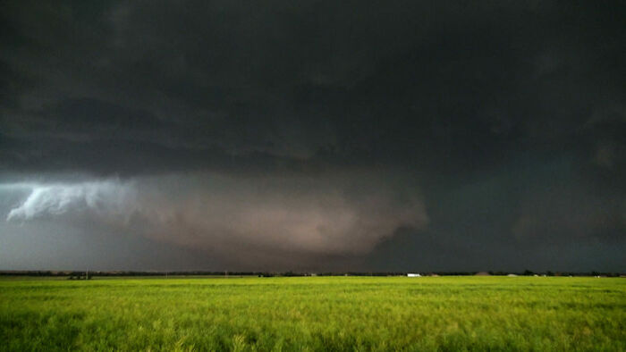 Dark storm clouds gathering over a green field illustrating incredible weather records and the powerful forces of nature.