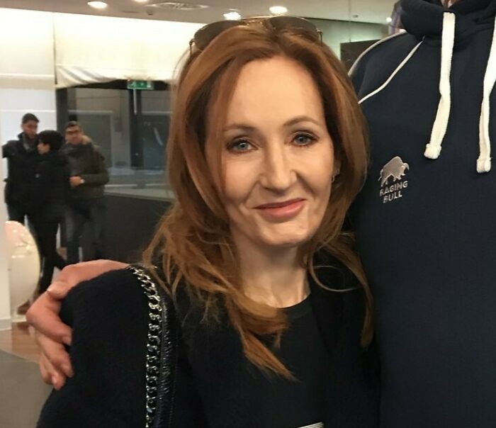 J.K. Rowling smiling indoors, interacting with someone, related to Harry Potter event and transgender community apology.