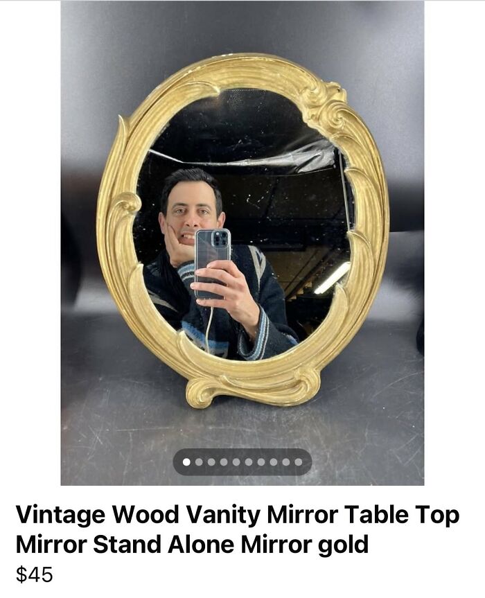 Man taking a selfie reflected in an ornate vintage wood vanity mirror with a gold frame for sale.