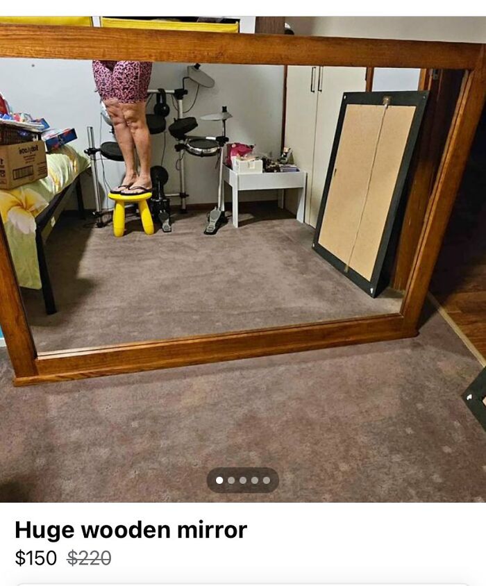 Large wooden mirror for sale showing the reflection of a person standing on a yellow stool in a bedroom setting.