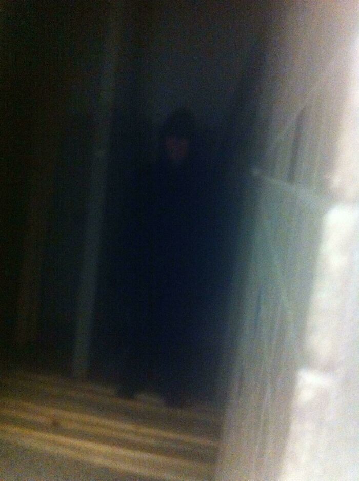 Blurry dark figure standing at the top of a staircase in a dimly lit, eerie setting, evoking creepy photo vibes.
