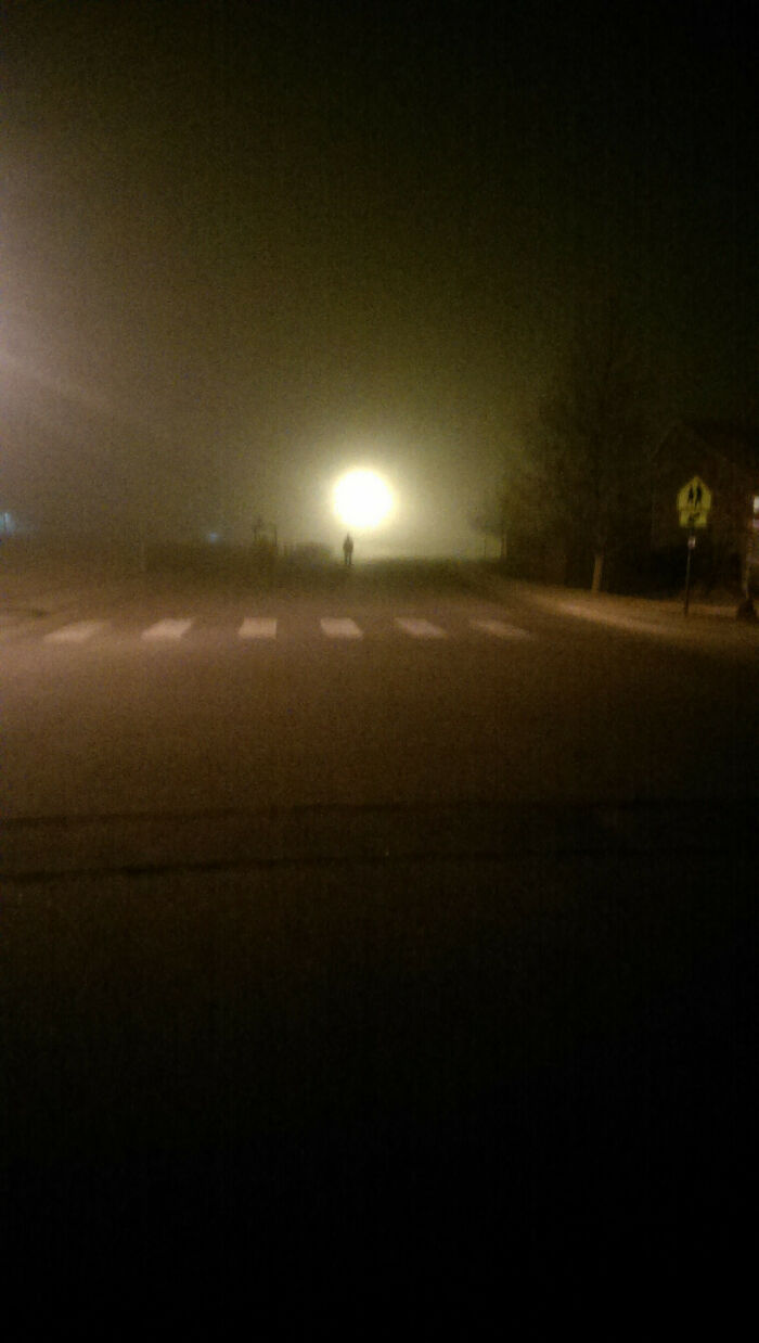 Silhouetted figure standing by a bright light on a foggy street at night, creating a creepy photo moment.