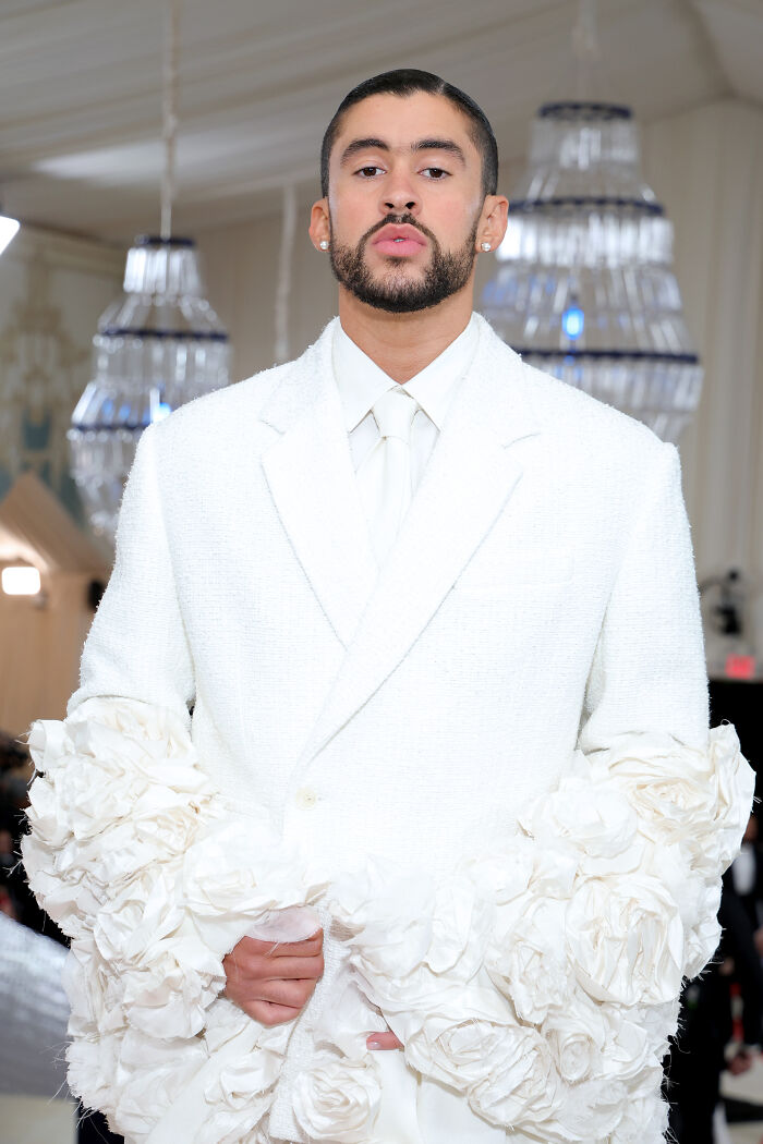 Handsome man in white suit with floral details posing confidently in a luxurious setting, embodying elegance and style.