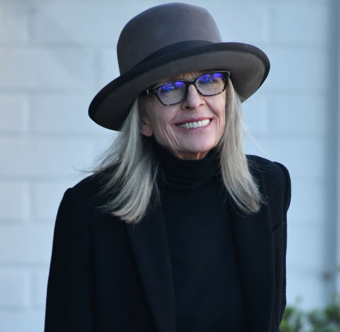 Diane Keaton wearing a gray hat and glasses, smiling outdoors in a black outfit, related to Diane Keaton cause revealed news.
