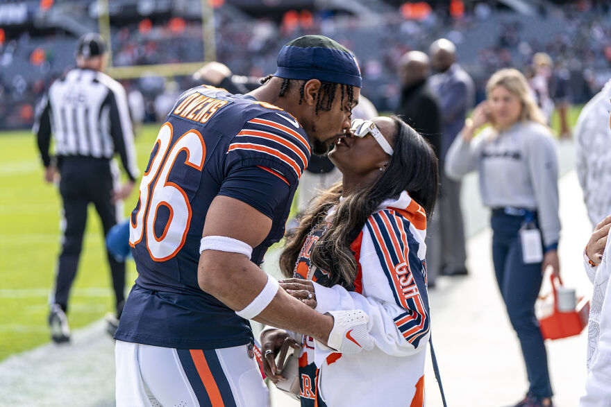 Jonathan Owens in football uniform sharing a kiss with Simone Biles on the sidelines during a game. Jonathan Owens in football uniform sharing a kiss with Simone Biles on the sidelines during a game.