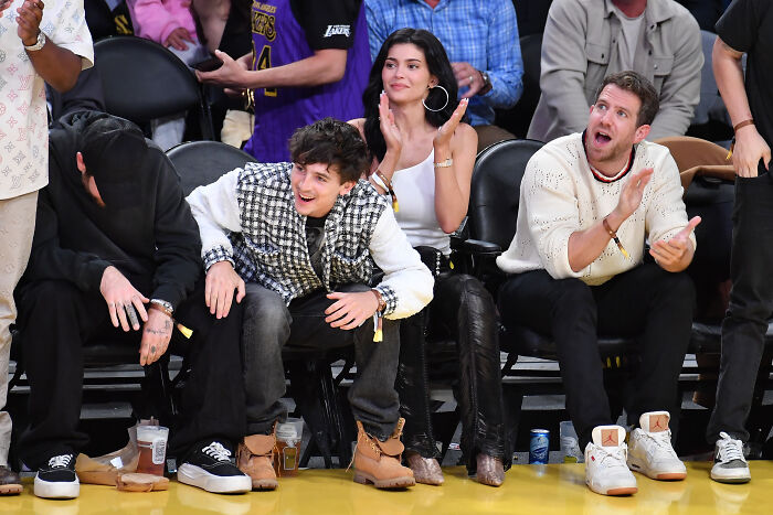 Timoth&eacute;e Chalamet and Kylie Jenner seated courtside at a basketball game with other spectators around them.