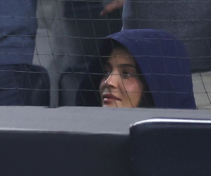 Kylie Jenner in a dark hood looking through a netted barrier during a public event, capturing sympathy after viral photos.