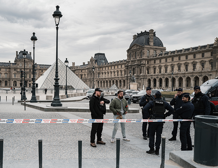 Police officers and bystanders gathered near the Louvre, discussing security after notorious jewel thief alerts on smuggling trick.