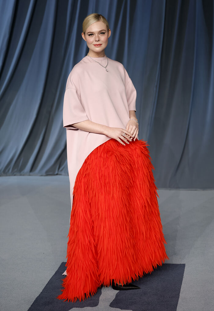 Woman wearing a pink top and bright red feathered skirt at the 2025 Academy Museum Gala red carpet event.