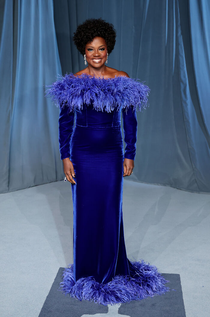 Elegant woman in a blue feathered gown posing at the 2025 Academy Museum Gala red carpet event.