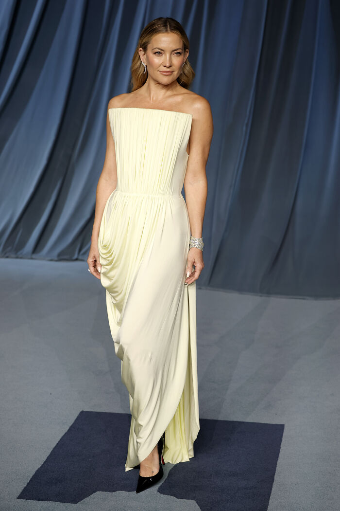 Woman in a pale yellow strapless gown posing on the 2025 Academy Museum Gala red carpet with elegant jewelry and black heels.