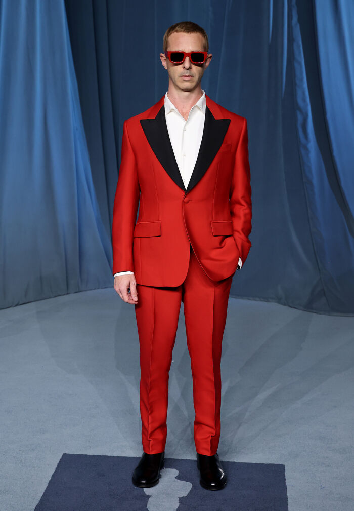 Man in a red suit and sunglasses posing on the red carpet at the 2025 Academy Museum Gala fashion event.