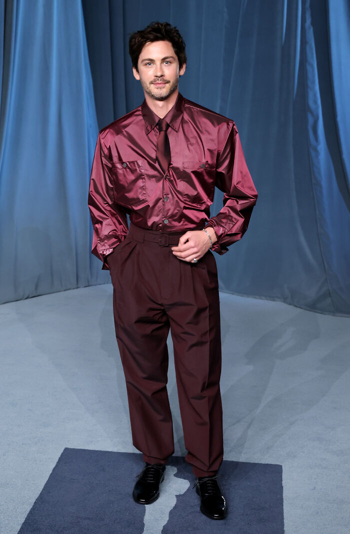 Man wearing shiny burgundy shirt and matching pants posing on the Academy Museum Gala red carpet fashion event.