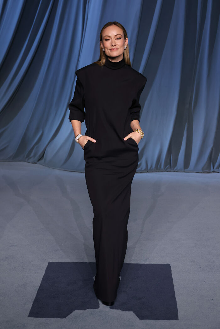 Woman wearing a sleek black gown and gold bracelets posing on the 2025 Academy Museum Gala red carpet.