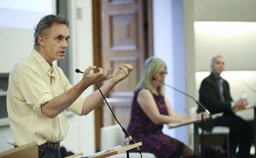 Jordan Peterson speaking passionately at a podium during a discussion on his net worth figures. Jordan Peterson speaking passionately at a podium during a discussion on his net worth figures.