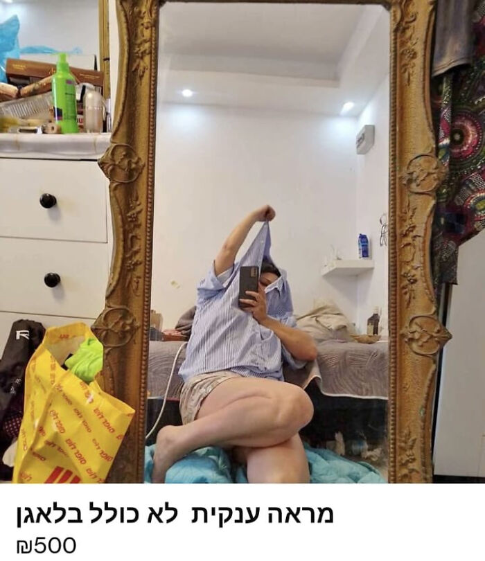 Person humorously covering face with shirt while sitting in front of a large ornate mirror, reflection selling the mirror.