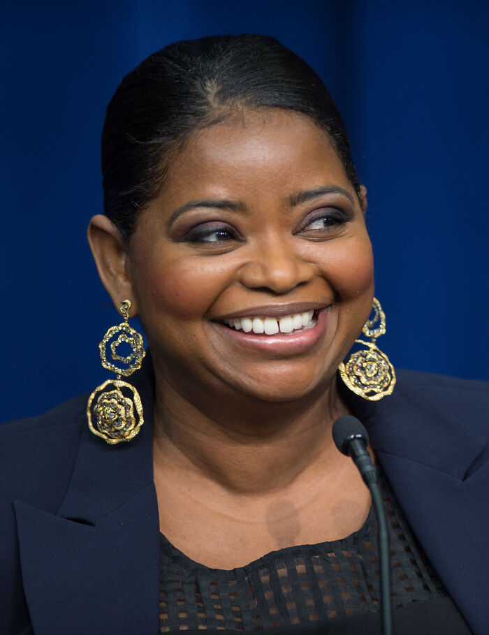 Smiling Hollywood star with gold earrings and dark blazer speaking at a microphone, representing fame after 30 success.