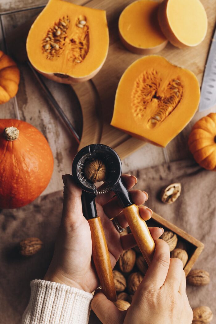 Hands cracking a walnut with autumn pumpkins and butternut squash halves on a wooden surface for cozy cake recipe.