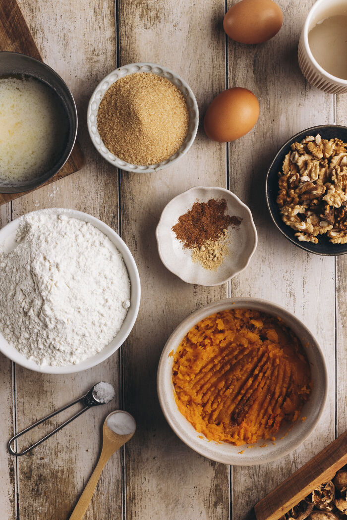 Butternut squash, spices, flour, sugar, eggs, and nuts arranged on a wooden table for autumn cake recipe.