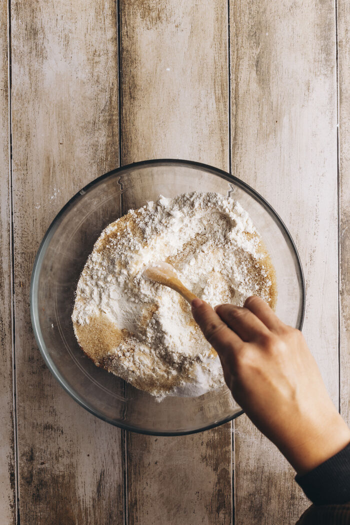 Hand stirring dry ingredients in a glass bowl preparing for a cozy butternut squash autumn cake recipe with cinnamon.