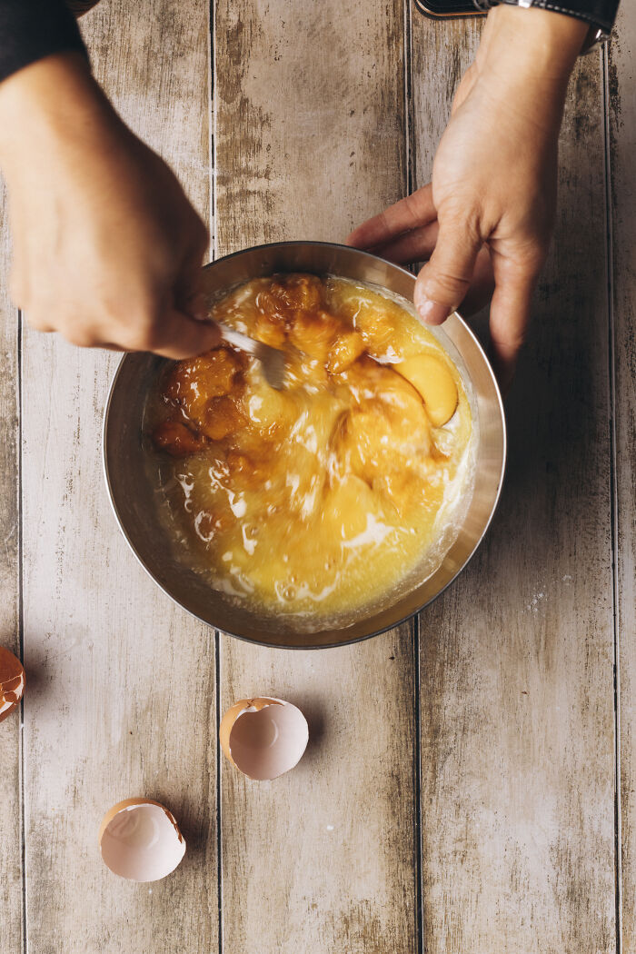 Hands mixing butternut squash and eggs in a bowl for a cozy autumn cake recipe with warm cinnamon flavors.