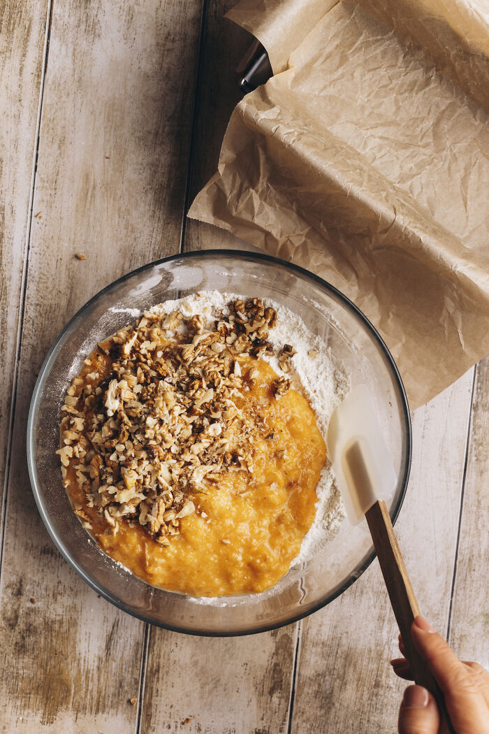 Mixing ingredients for a cozy butternut squash autumn cake with chopped nuts in a glass bowl on a wooden table.