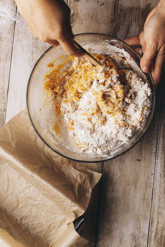Mixing butternut squash cake batter with flour in a glass bowl on a wooden surface for an autumn recipe.