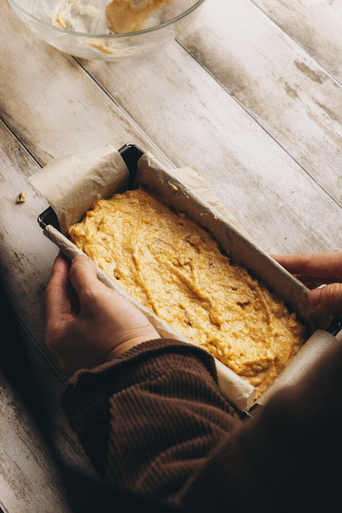 Hands holding a parchment-lined loaf pan filled with butternut squash autumn cake batter ready to bake.