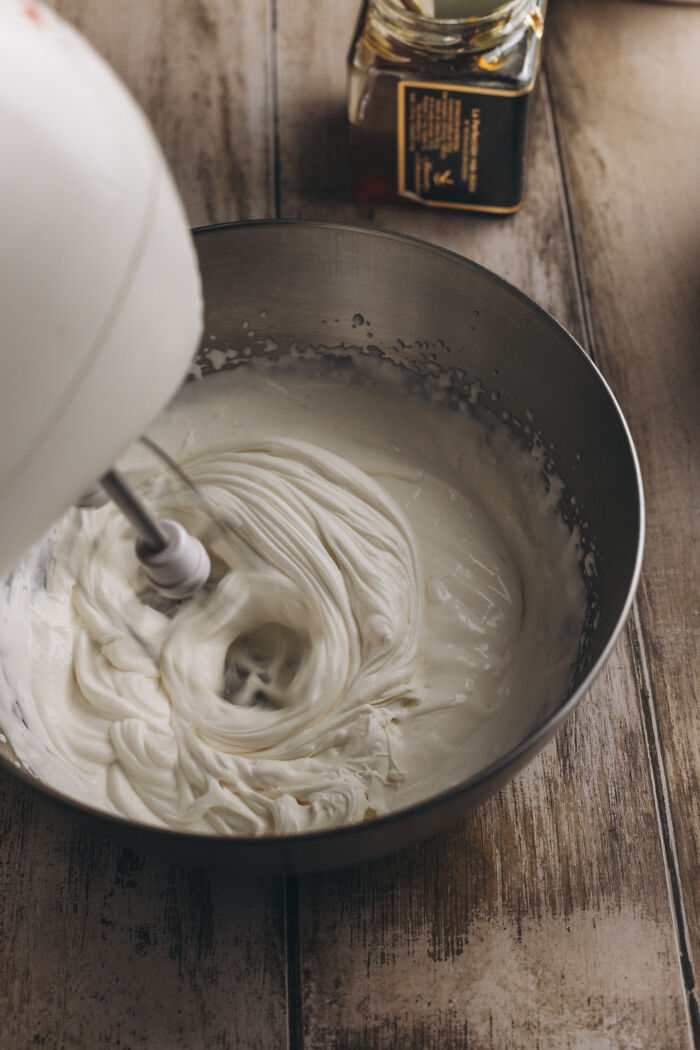 Hand mixer whipping creamy frosting in a bowl preparing for cozy butternut squash autumn cake recipe with cinnamon.