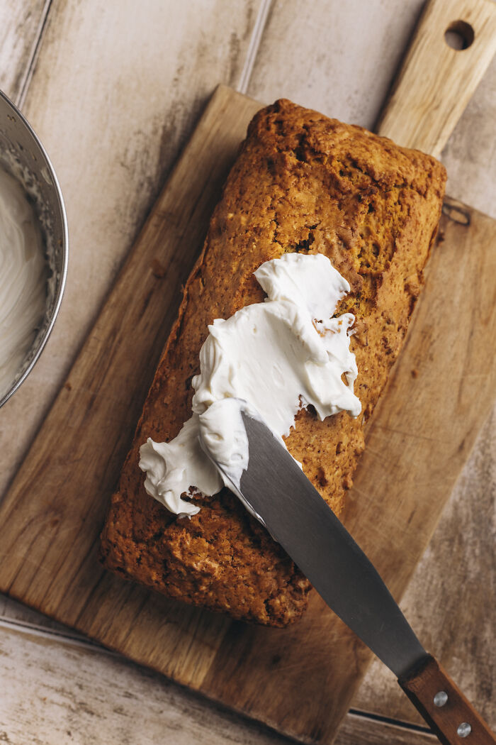 Butternut squash autumn cake on wooden board being spread with creamy frosting with a knife.