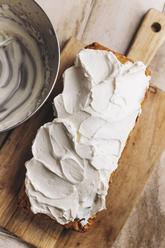 Butternut squash autumn cake on wooden board being frosted with creamy cinnamon-spiced icing in a metal bowl nearby