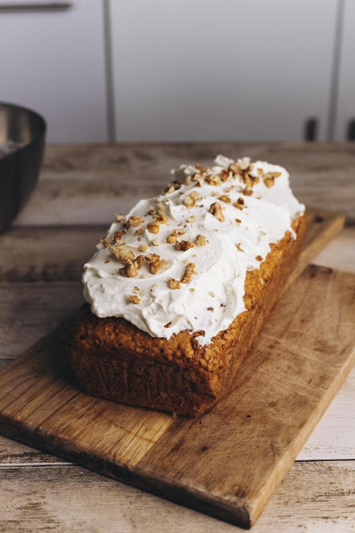 Butternut squash autumn cake topped with creamy frosting and chopped walnuts on a wooden cutting board.