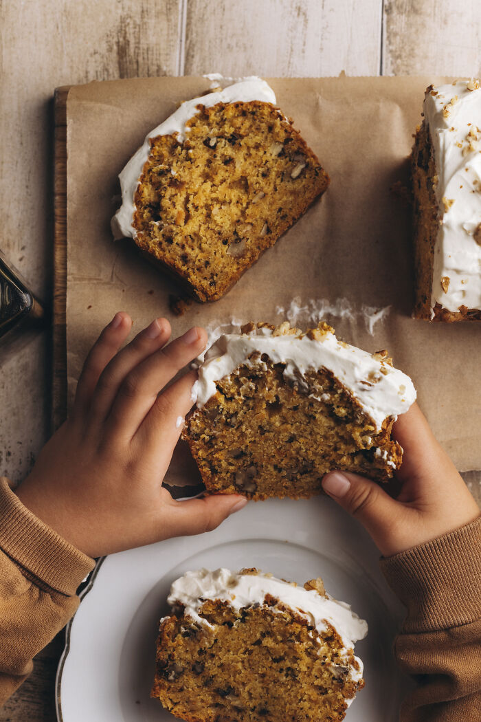 Hands holding a cozy butternut squash autumn cake slice with cinnamon and cream frosting on a wooden table.